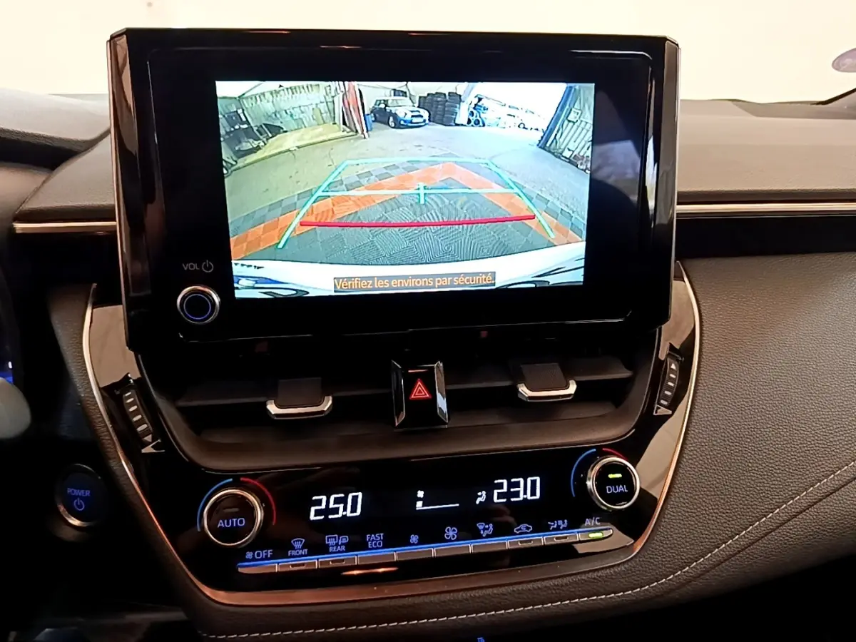 Vue intérieure du tableau de bord de la Toyota Corolla hybride 2022 avec écran de caméra de recul et commandes de climatisation digitales.