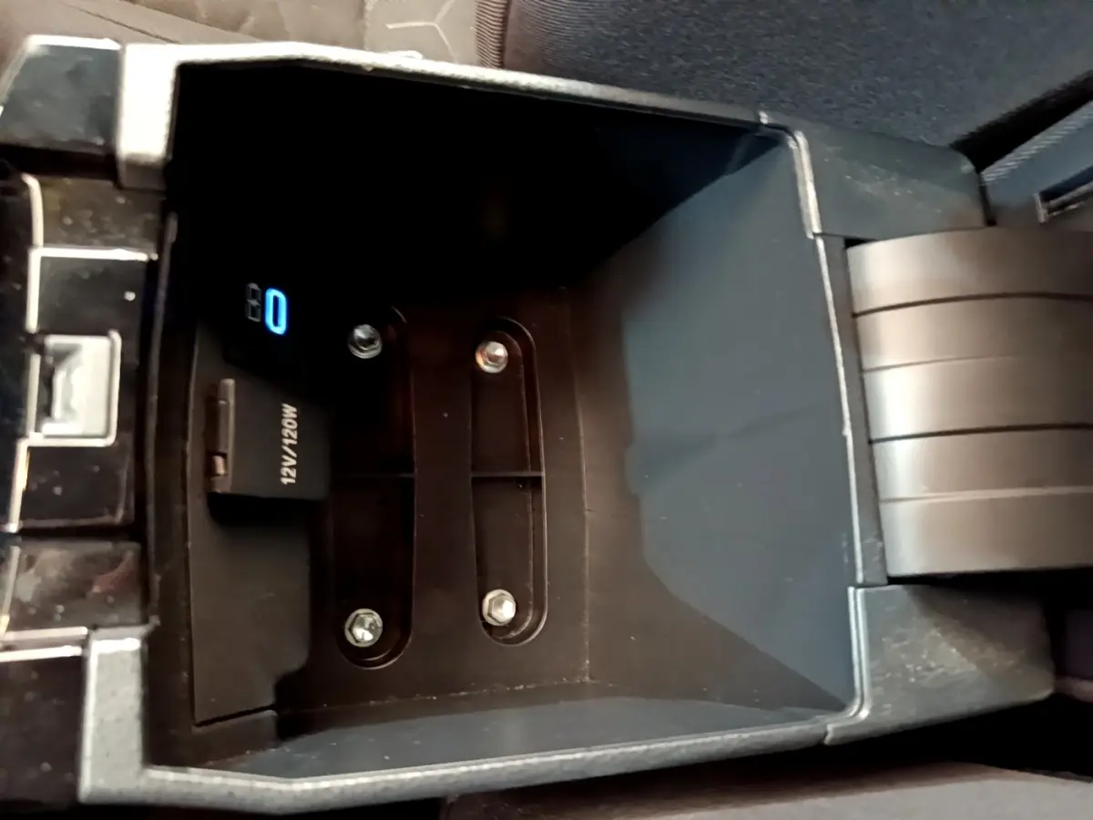 Vue en plongée sur le compartiment de rangement central noir de la Toyota Corolla hybride 2022 avec prise 12V visible.