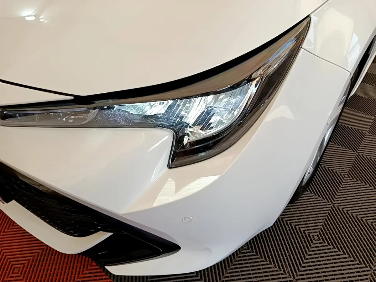 Gros plan sur l'avant droit blanc de la Toyota Corolla hybride 2022, mettant en valeur le phare LED et la calandre noire.