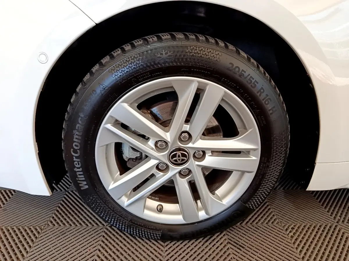 Gros plan sur la roue avant droite d'une Toyota Corolla blanche, jante alliage argentée et pneu hiver visible.