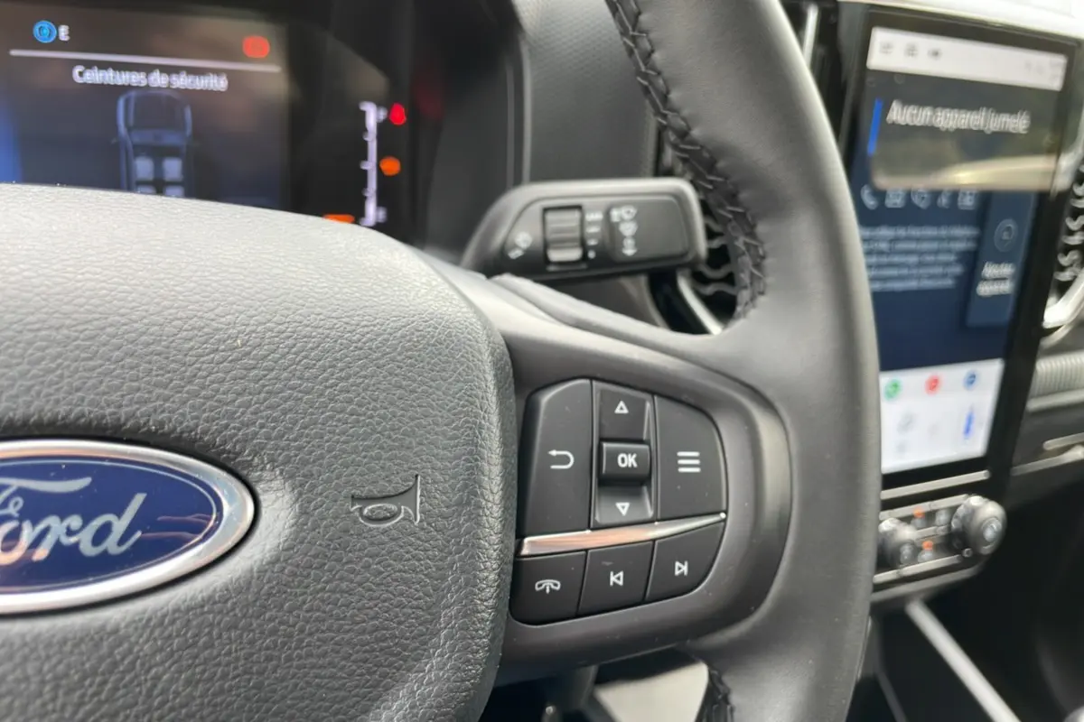 Gros plan sur le volant cuir multifonctions du Ford Ranger gris carbone, avec écran tactile et commandes au volant visibles.