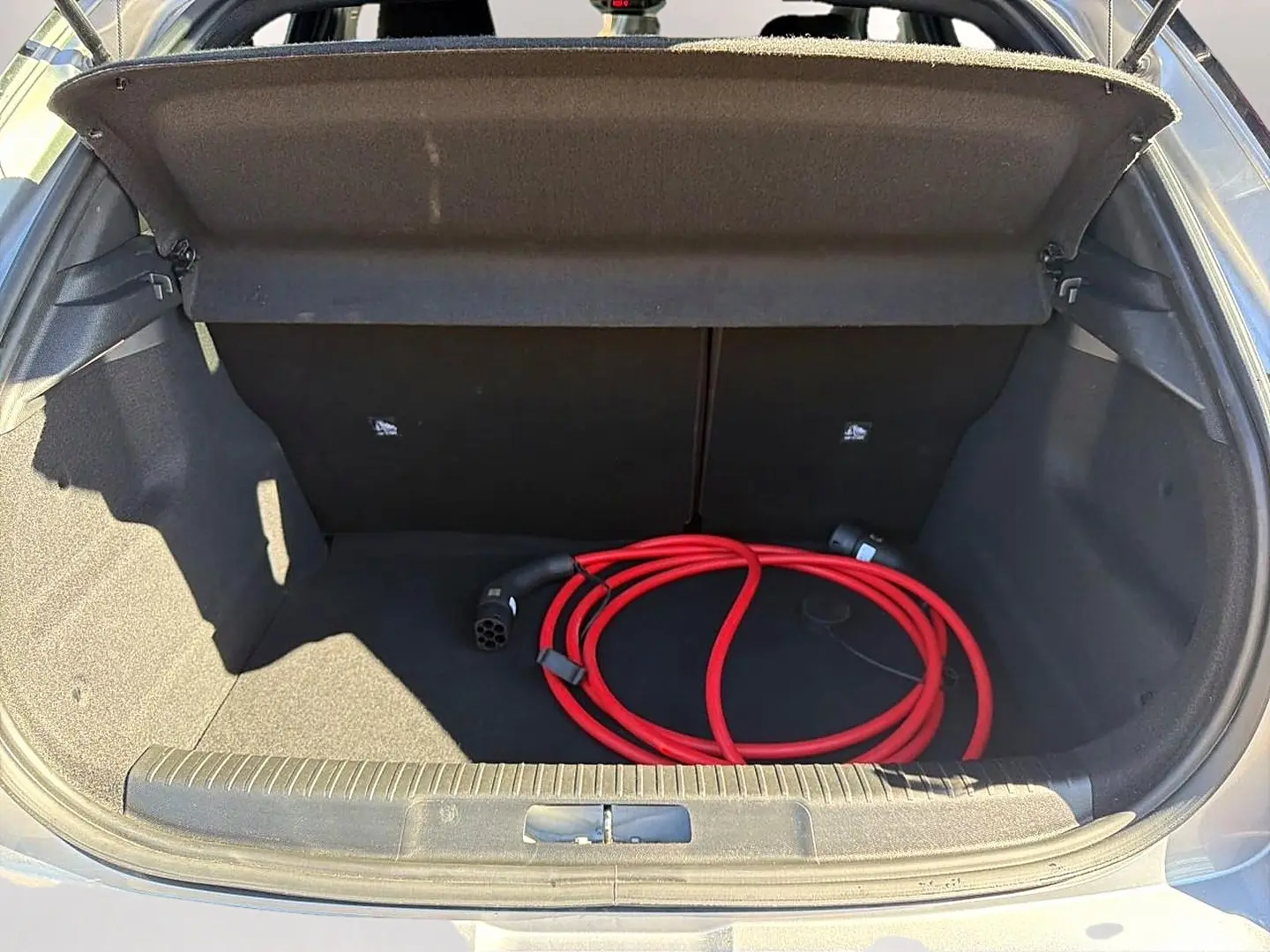 Coffre ouvert d’un Opel Mokka Electric gris 2025 avec câble de recharge électrique rouge enroulé.