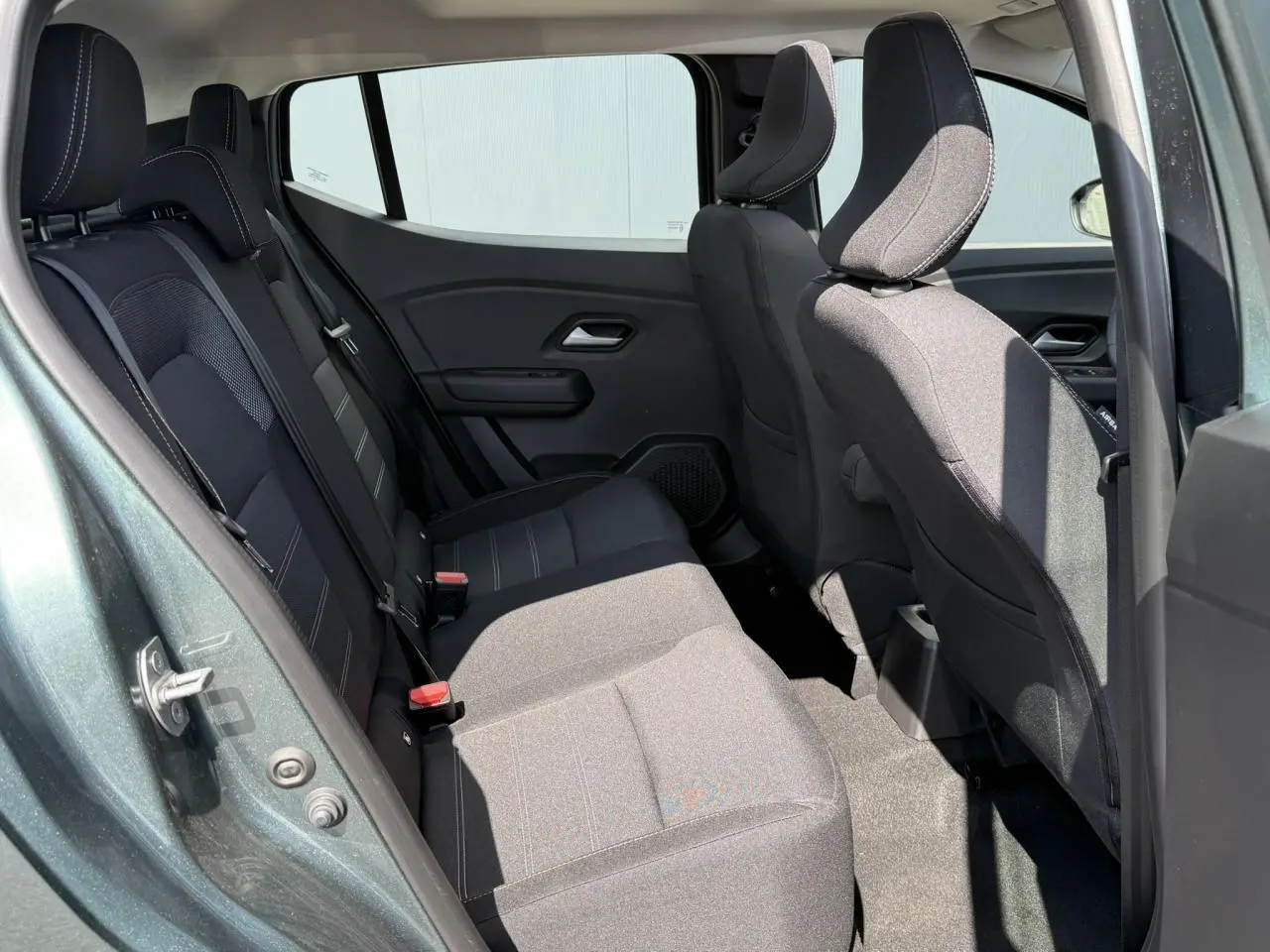 Vue côté gauche de l'habitacle arrière du Dacia Sandero Stepway Vert Cèdre, sièges tissu noir avec surpiqûres grises.
