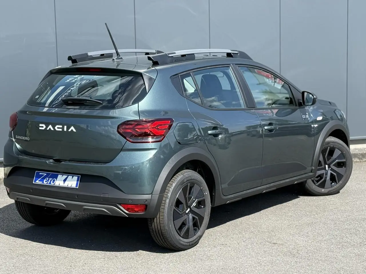 Vue 3/4 arrière droite d'une Dacia Sandero Stepway Vert Cèdre avec barres de toit et jantes 16 pouces noires.