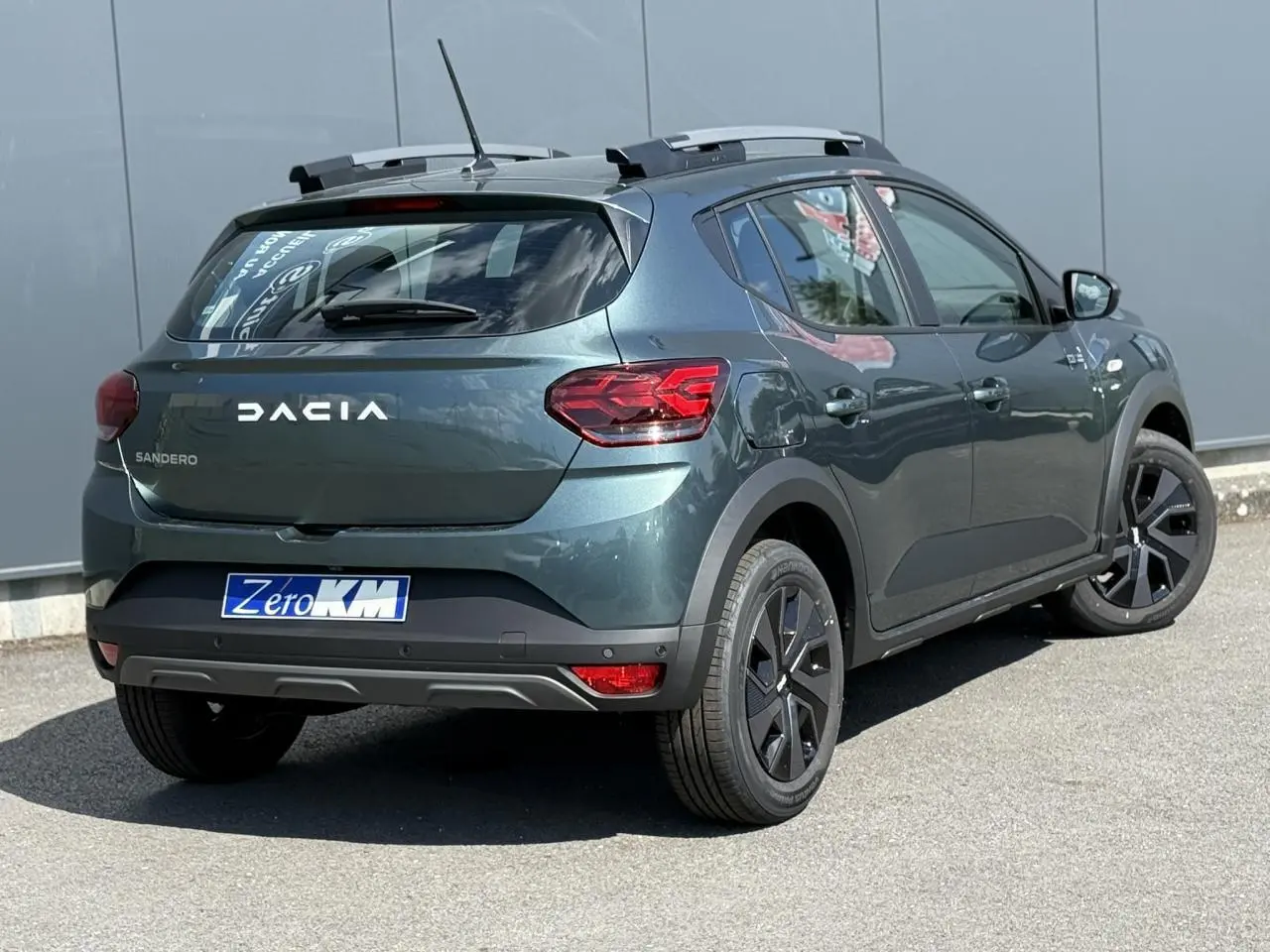 Vue 3/4 arrière droite d'une Dacia Sandero Stepway Vert Cèdre avec barres de toit et jantes 16 pouces noires.