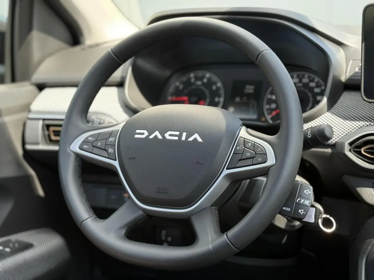 Gros plan sur le volant noir Dacia avec commandes intégrées, tableau de bord et partie de la console centrale visibles.