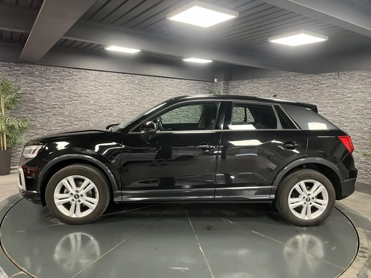 Profil côté gauche d'un Audi Q2 noir brillant 2023 dans un showroom avec jantes aluminium à 5 branches doubles.