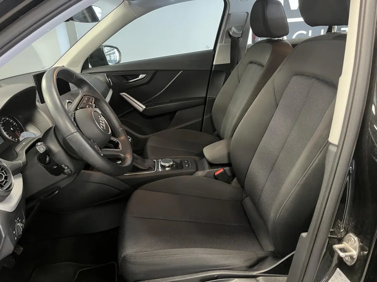 Vue intérieure côté conducteur de l'Audi Q2 2023 noire, montrant sièges tissu et volant multifonction cuir.