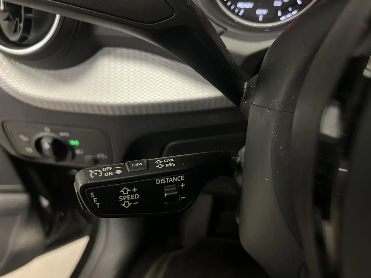 Gros plan sur la commande du régulateur adaptatif à gauche du volant d’un Audi Q2 noir 2023 Design.