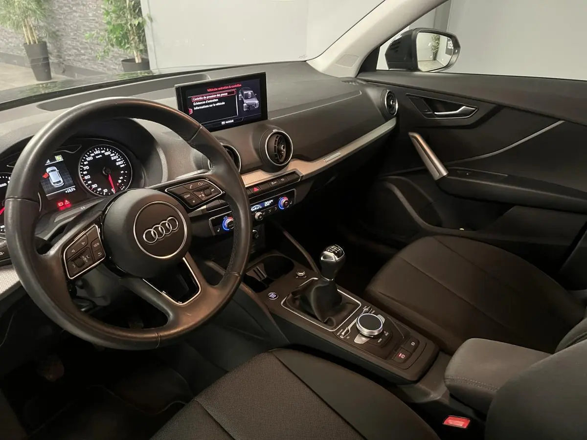 Intérieur Audi Q2 2023 vu côté conducteur, volant cuir, tableau de bord noir et levier de vitesse manuel.