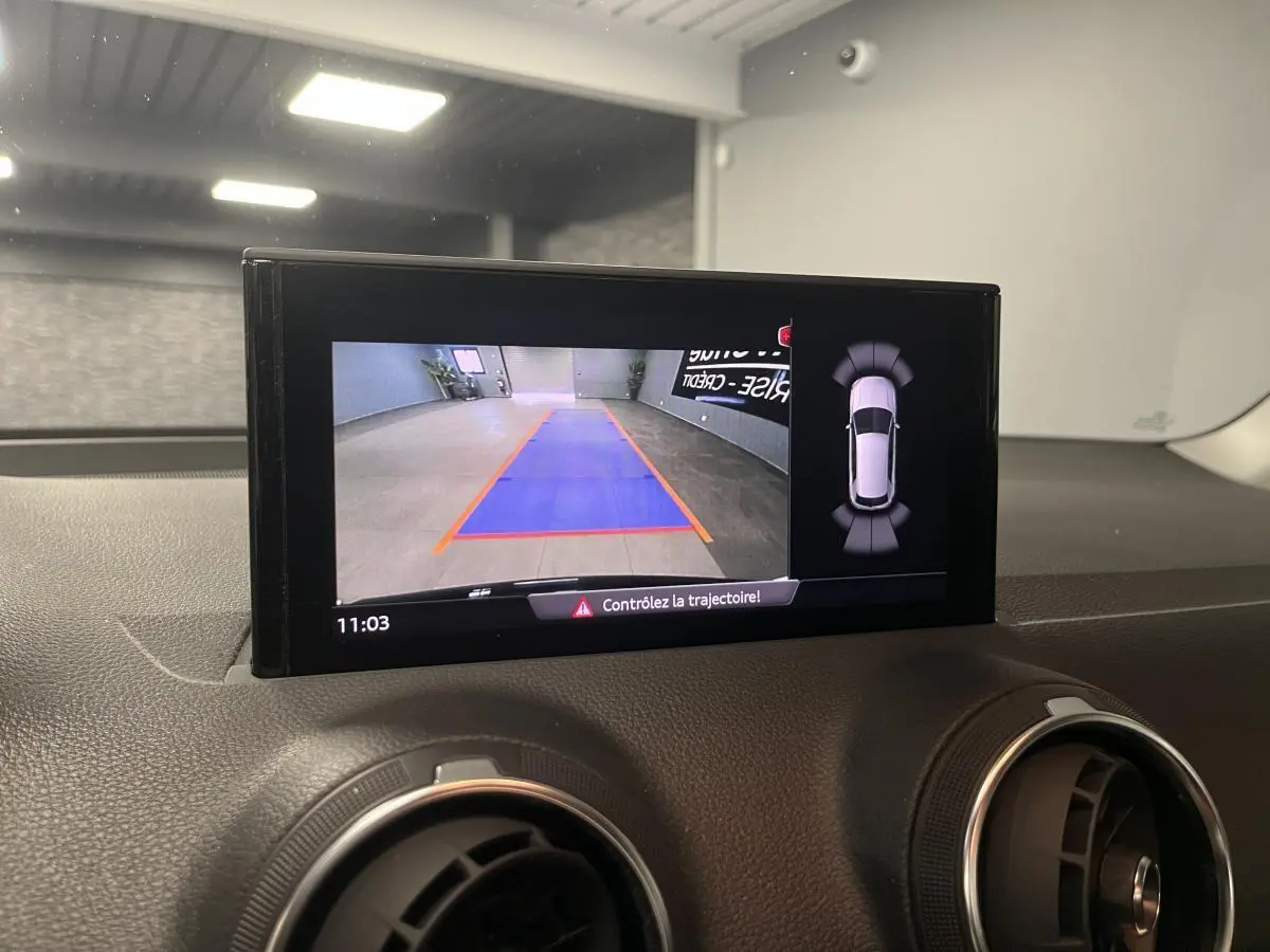 Écran central affichant la caméra de recul et l'aide au stationnement sur le tableau de bord noir de l'Audi Q2 2023