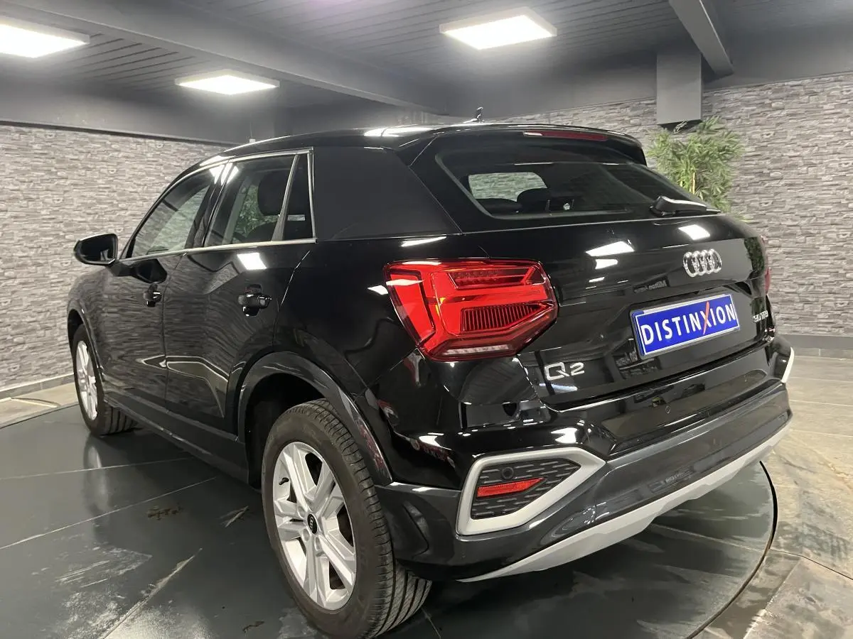 Audi Q2 noir brillant vue 3/4 arrière droit en intérieur avec feux arrière LED et jantes 17 pouces.