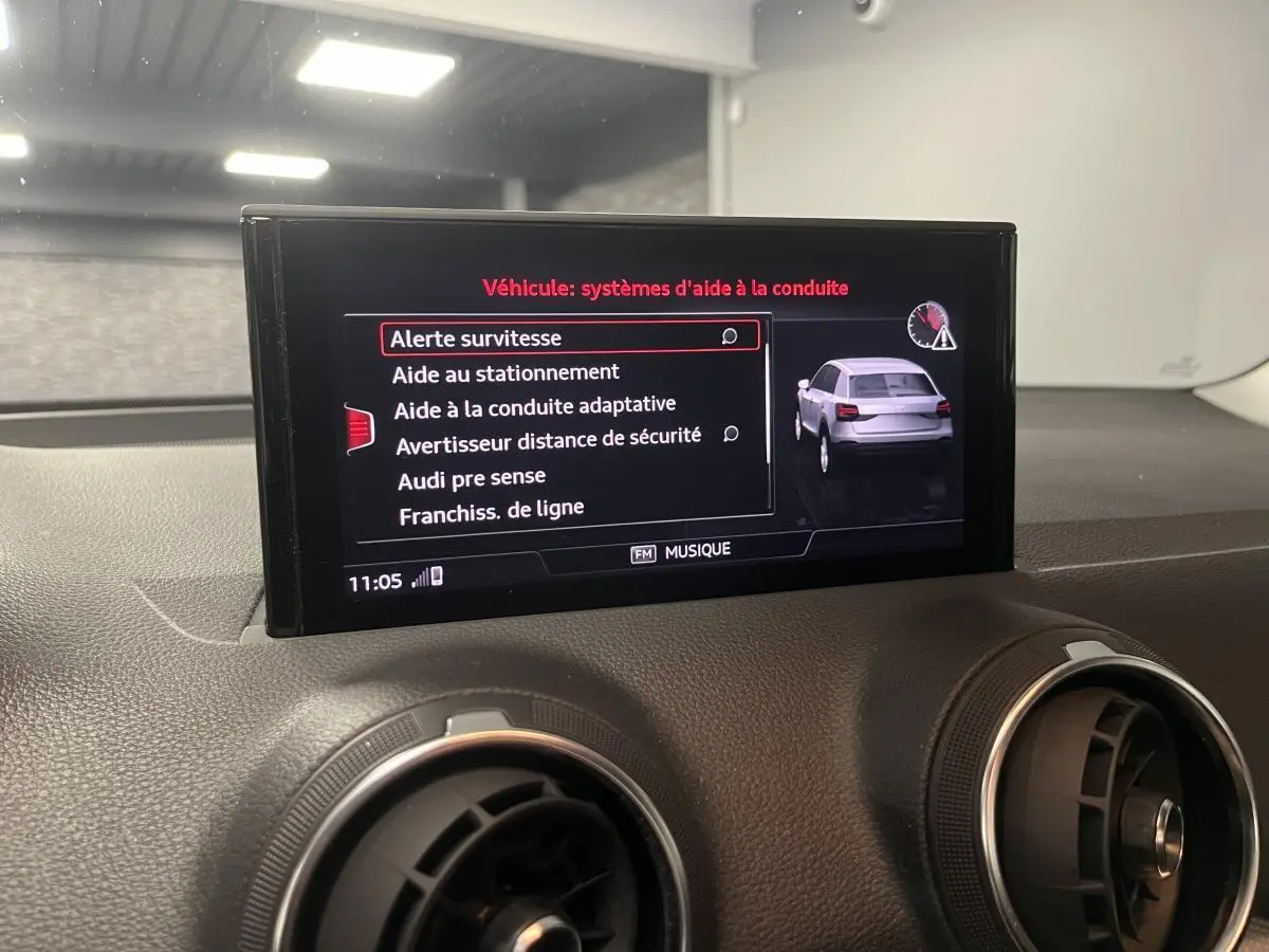 Écran central de l'Audi Q2 2023 affichant les aides à la conduite avec vue du tableau de bord noir.