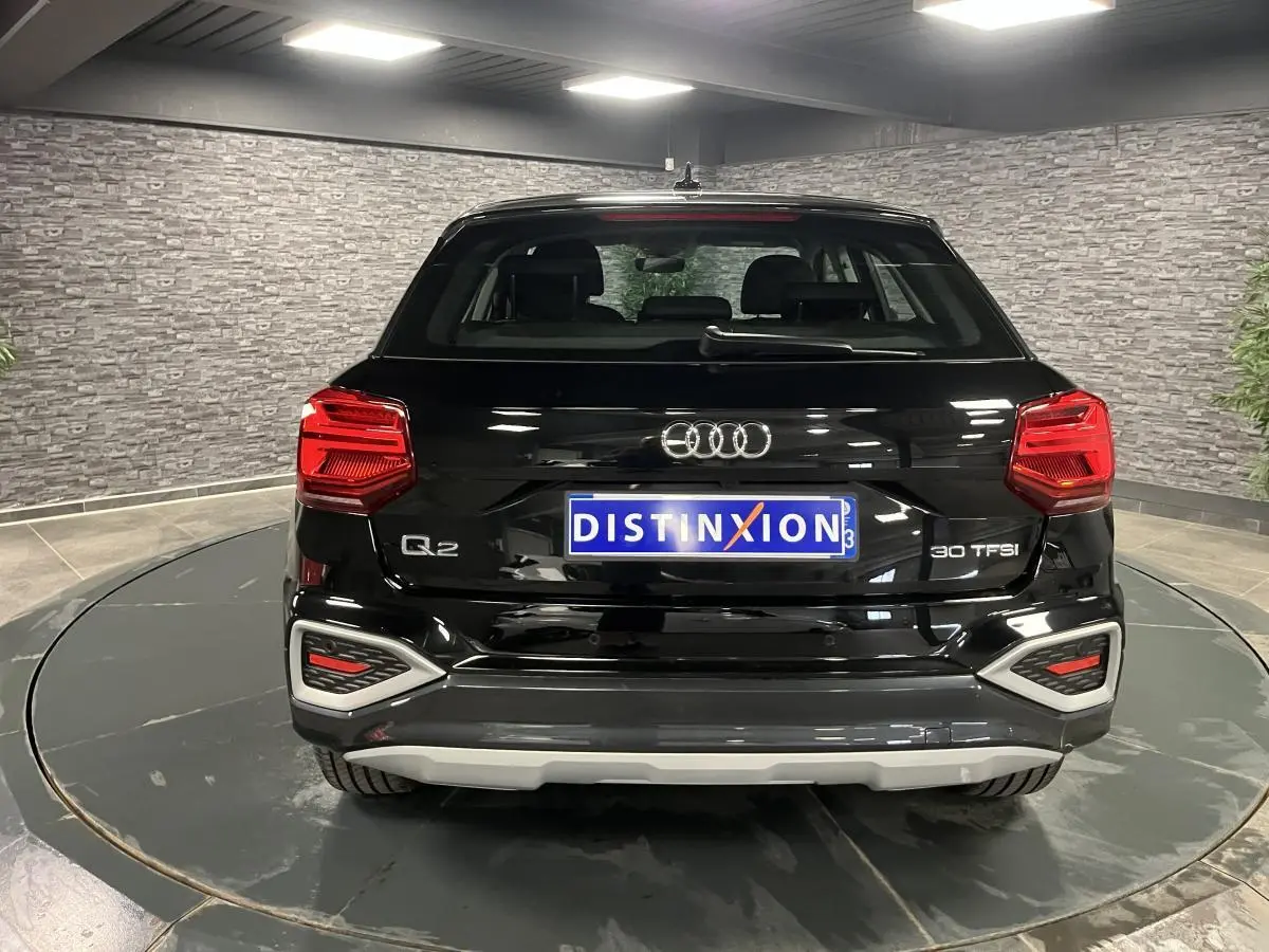 Vue arrière d'un Audi Q2 noir brillant 2023 avec feux LED et logo distinctif sur fond intérieur gris.