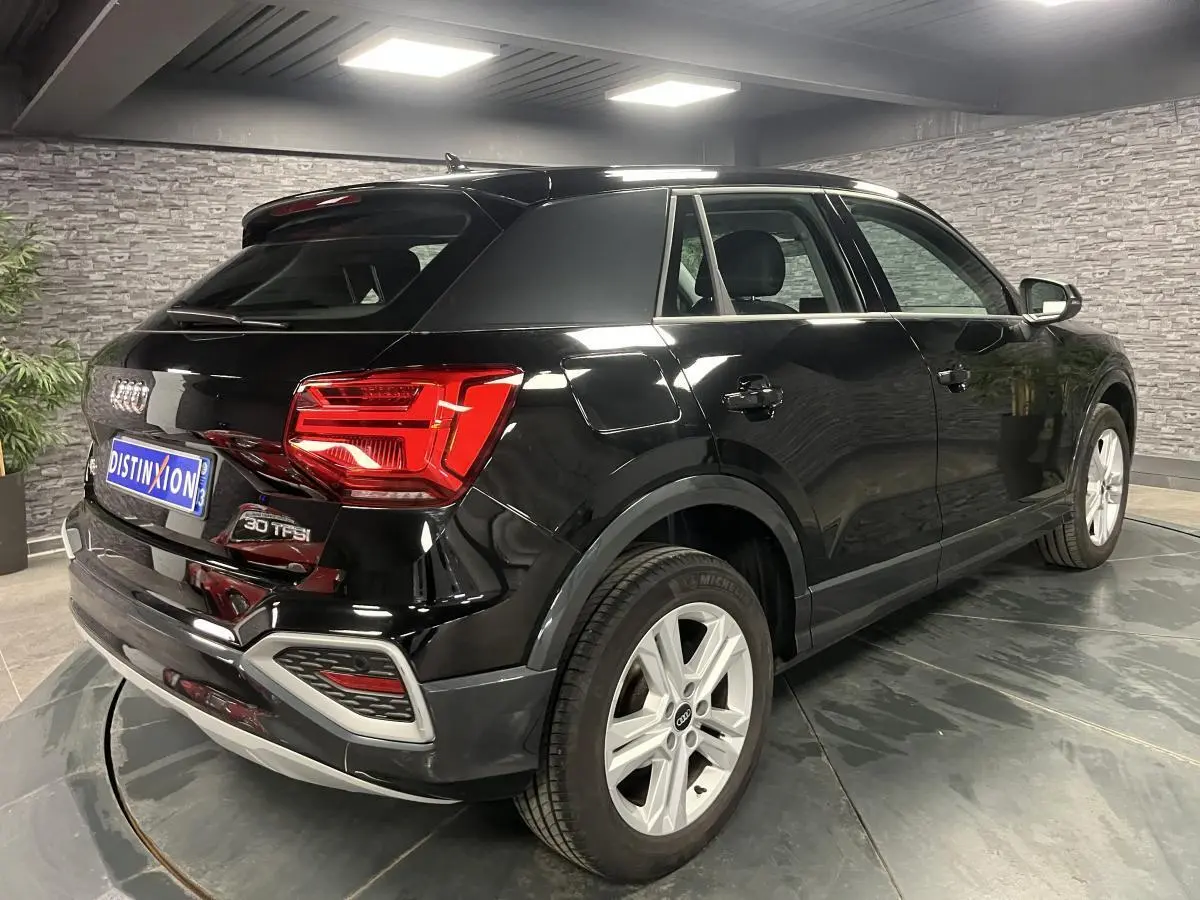 Audi Q2 noir brillant vue 3/4 arrière droit en intérieur avec jantes aluminium 5 branches doubles.