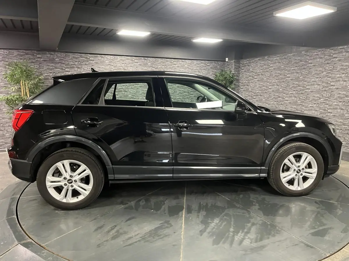 Audi Q2 noir brillant vue de profil côté gauche dans un showroom avec jantes aluminium à 5 branches doubles.