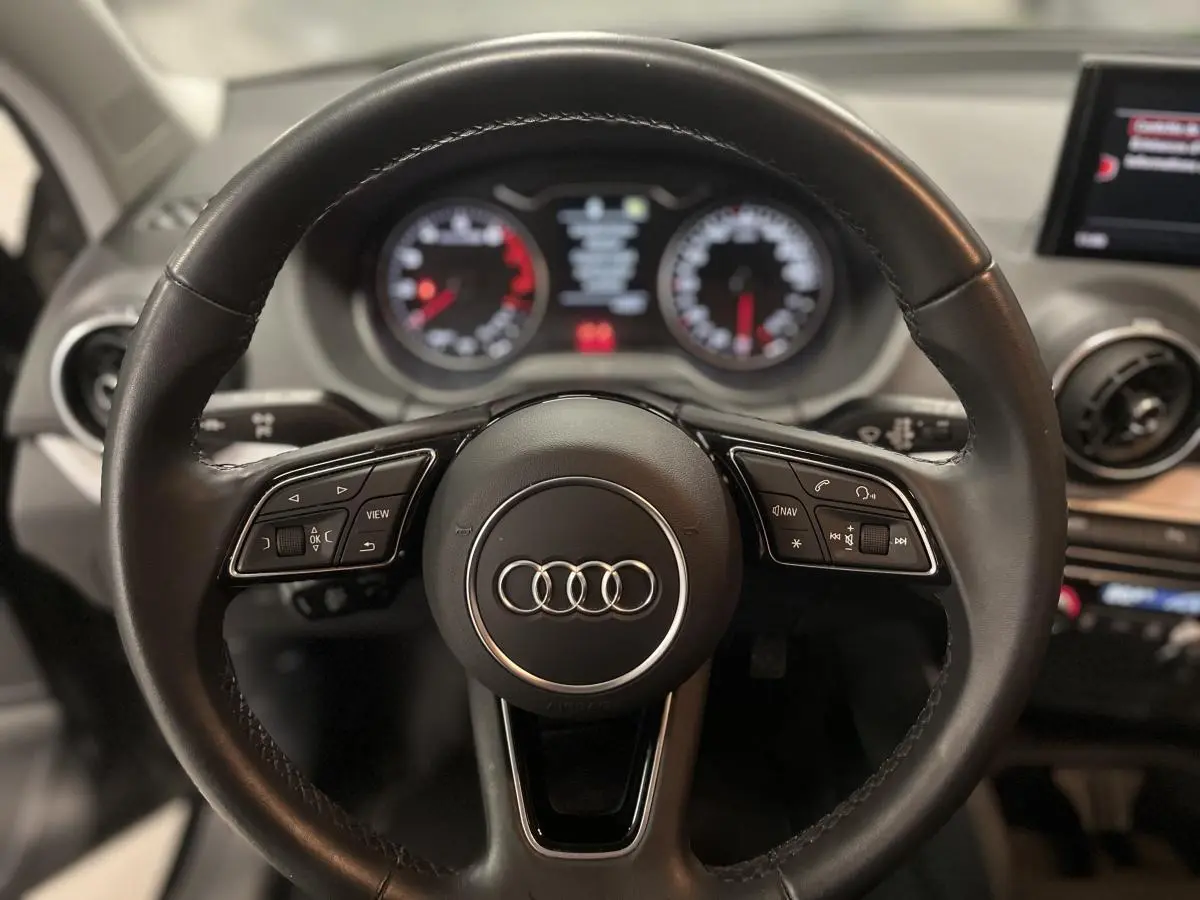Vue intérieure centrée sur le volant cuir multifonction de l'Audi Q2 1.0 30 TFSI Design 2023 noire, avec aérateurs ronds et écran MMI.