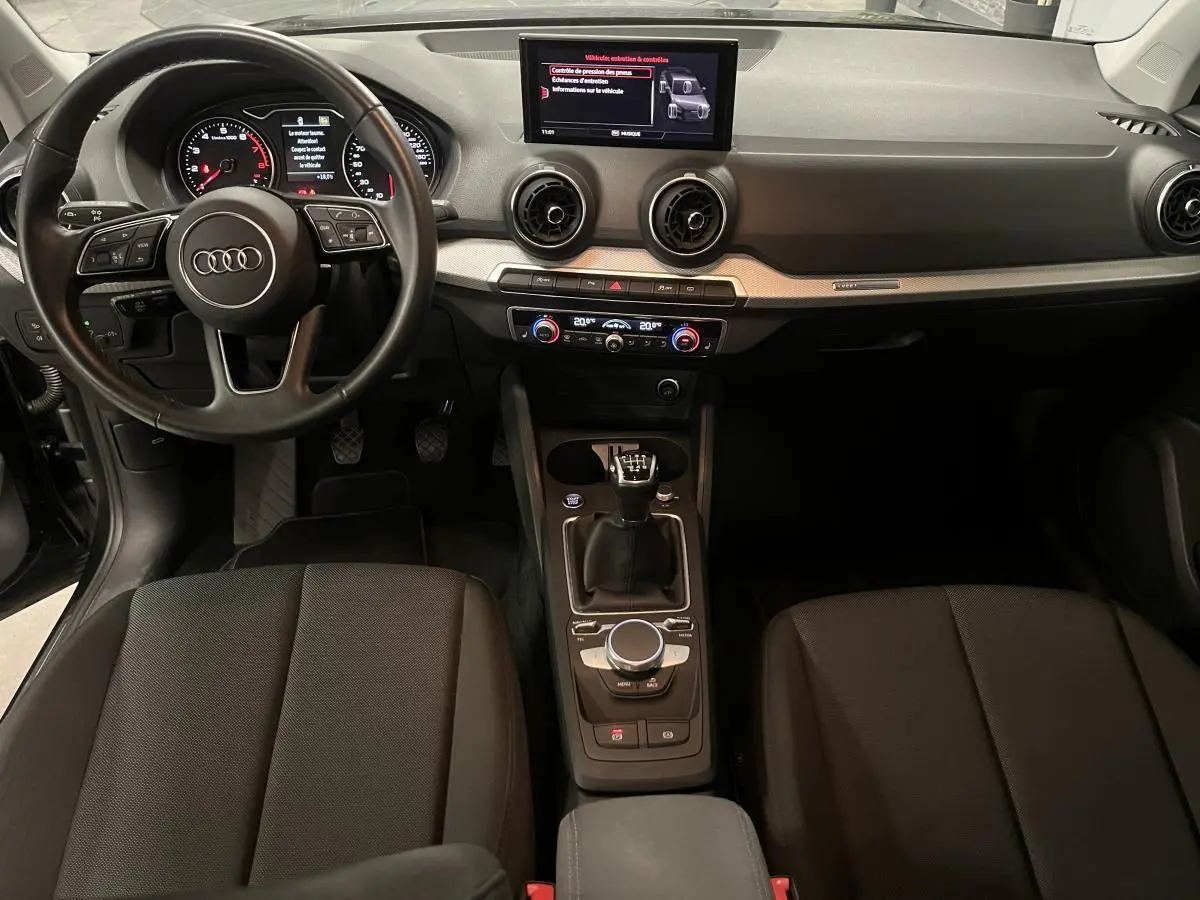 Vue intérieure avant de l'Audi Q2 2023 essence noire, volant cuir, tableau de bord moderne et boîte manuelle.