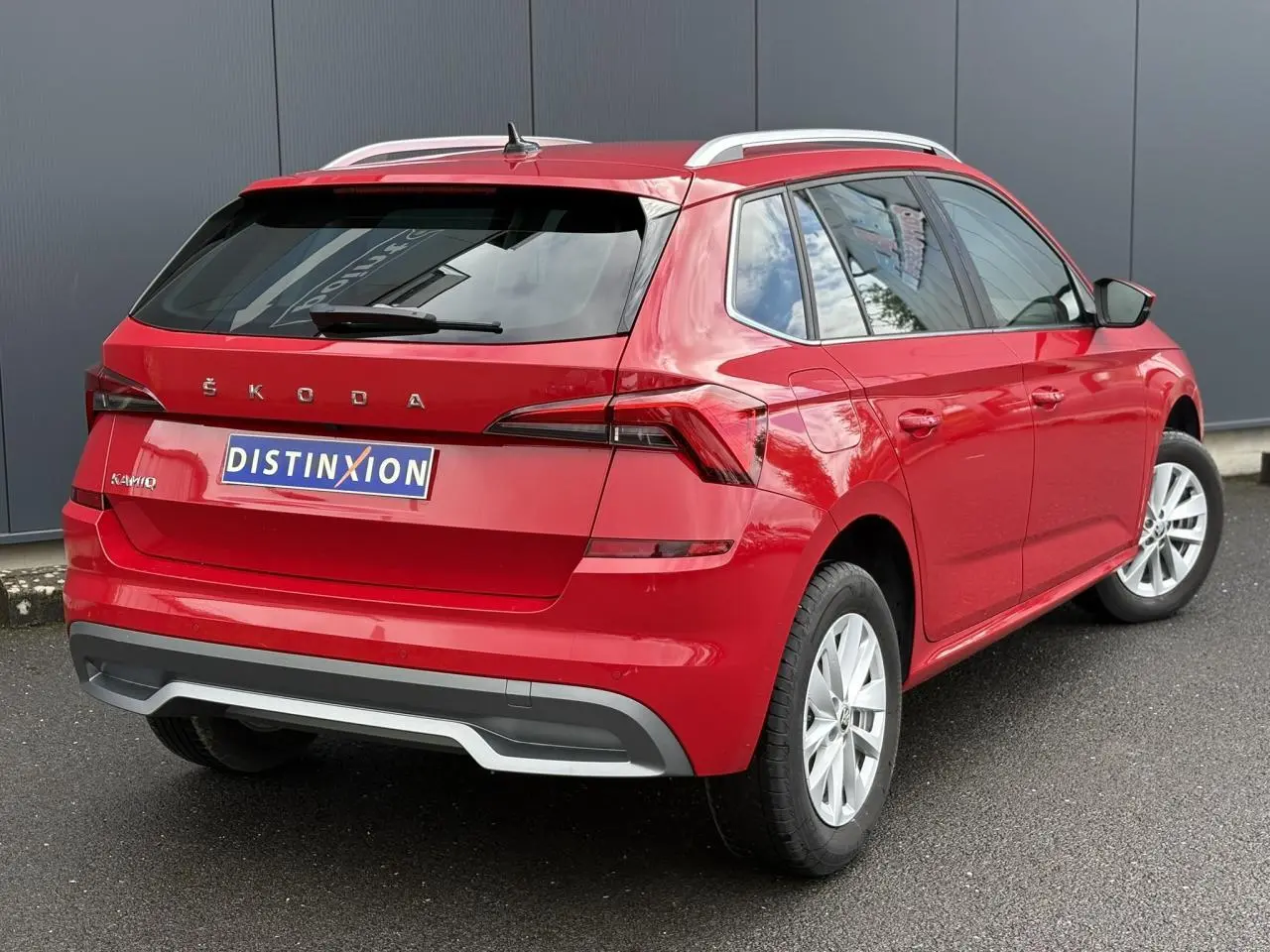 Vue 3/4 arrière droite d'un Skoda Kamiq rouge Velvet avec jantes alliage et barres de toit argentées.