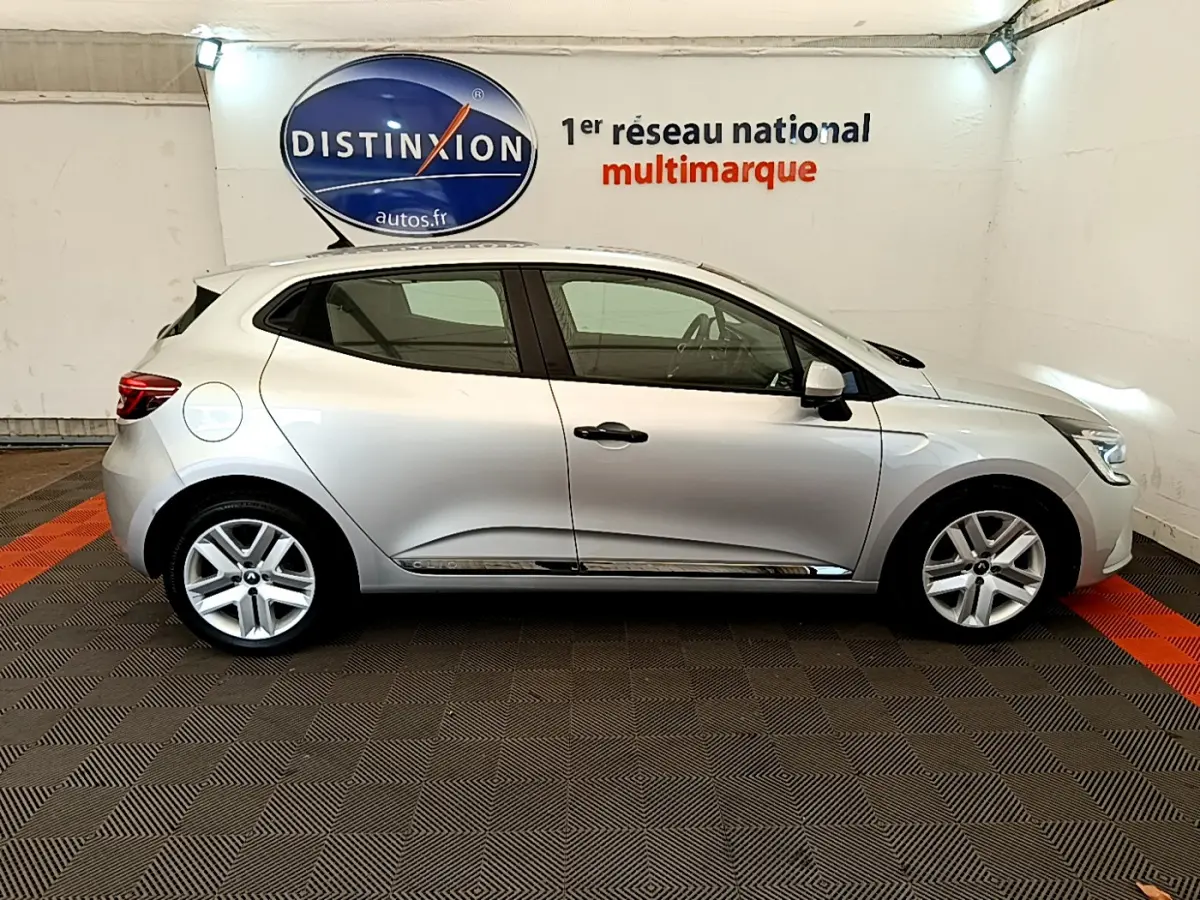 Profil côté gauche d'une Renault Clio Business TCe 100 gris clair, garée en intérieur sur sol à damier noir et rouge.