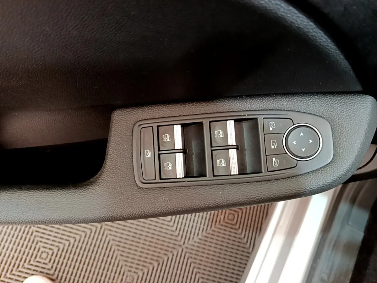 Gros plan sur la commande des vitres et rétroviseurs côté conducteur d'une Renault Clio Business gris clair de 2020.