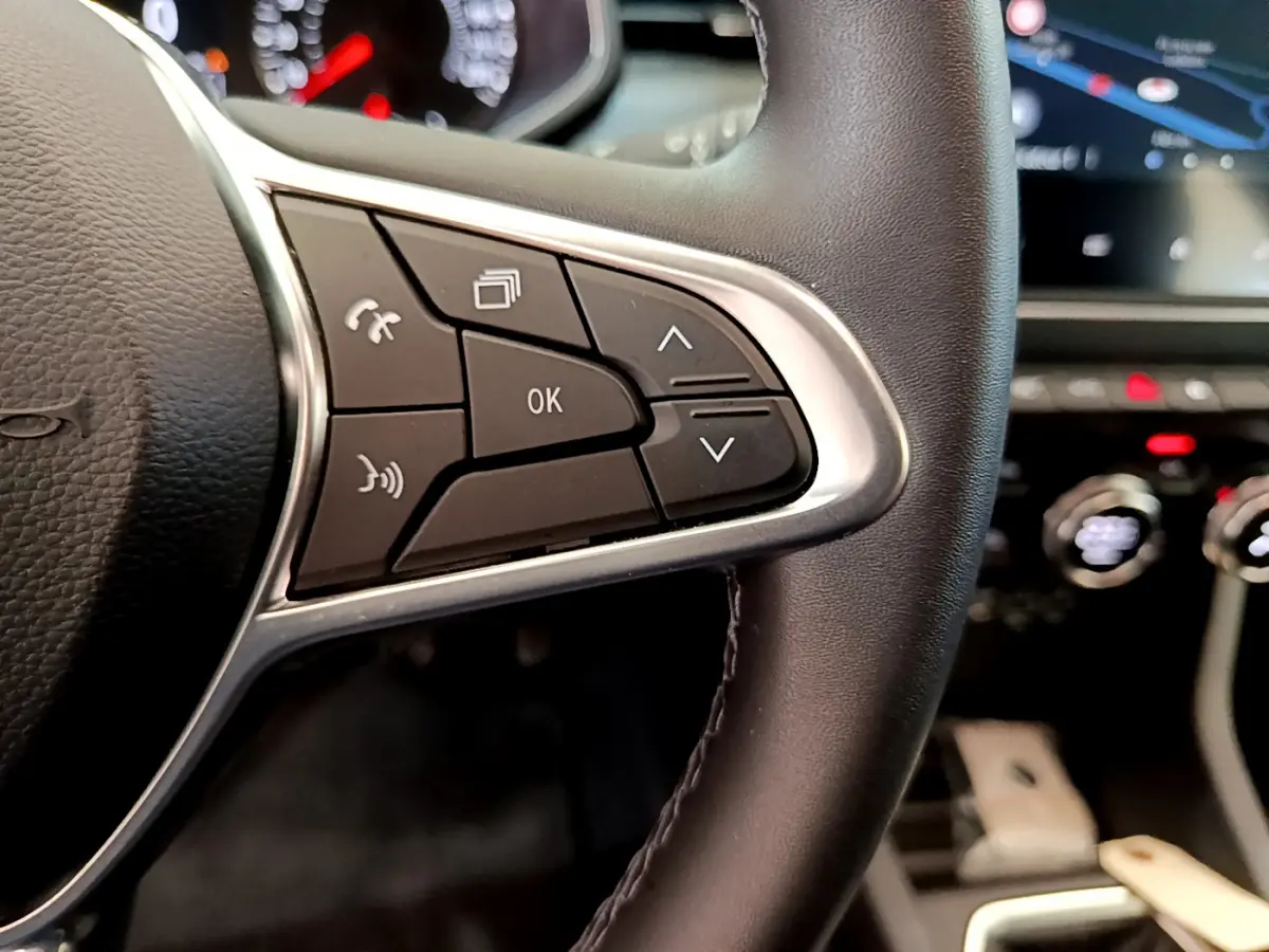 Gros plan sur les commandes du volant cuir synthétique de la Renault Clio Business TCe 100 2020, avec écran tactile en arrière-plan.