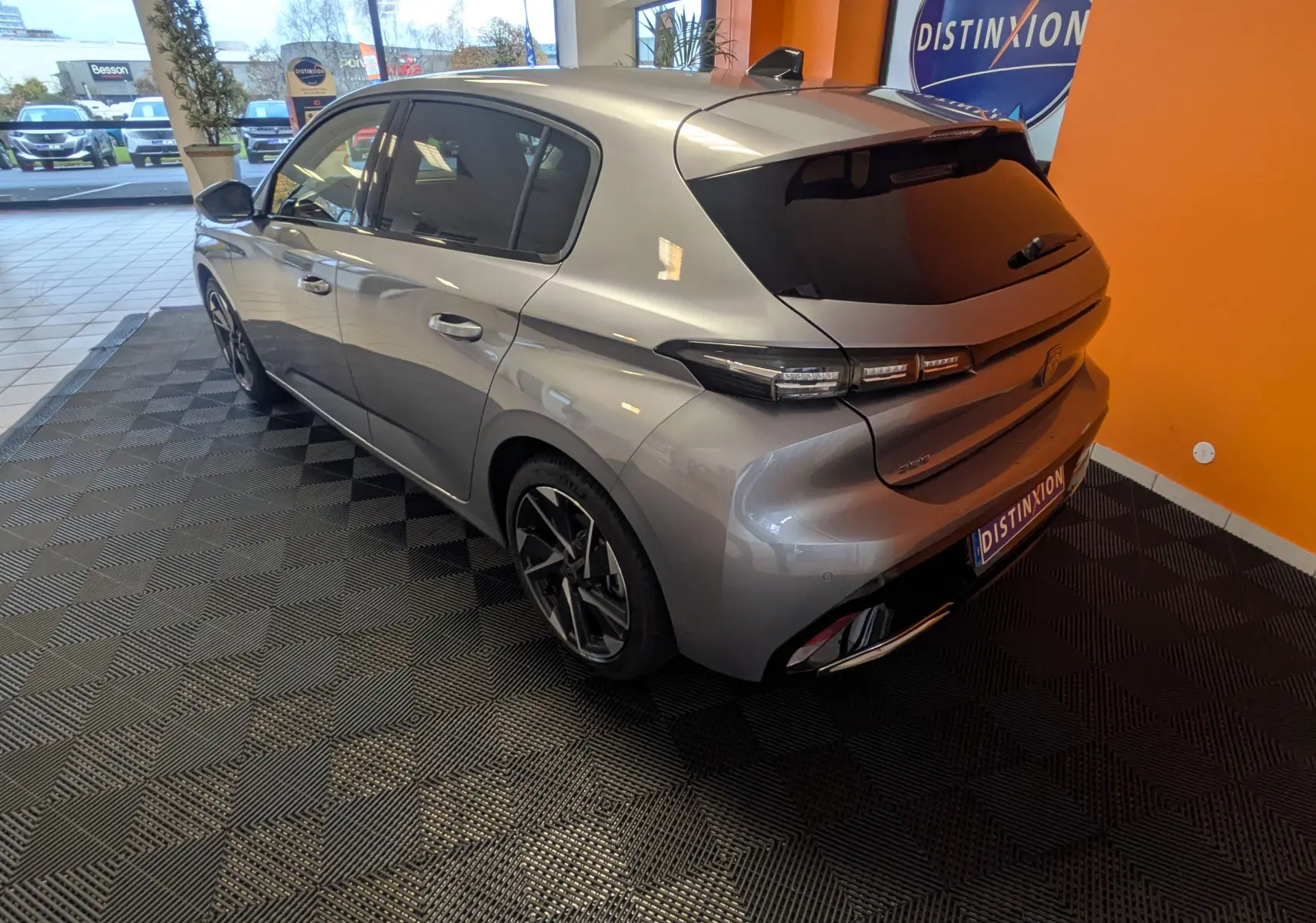 Vue 3/4 arrière droite d'une Peugeot 308 2025 gris Artense avec vitres teintées et jantes alliage noires en showroom.