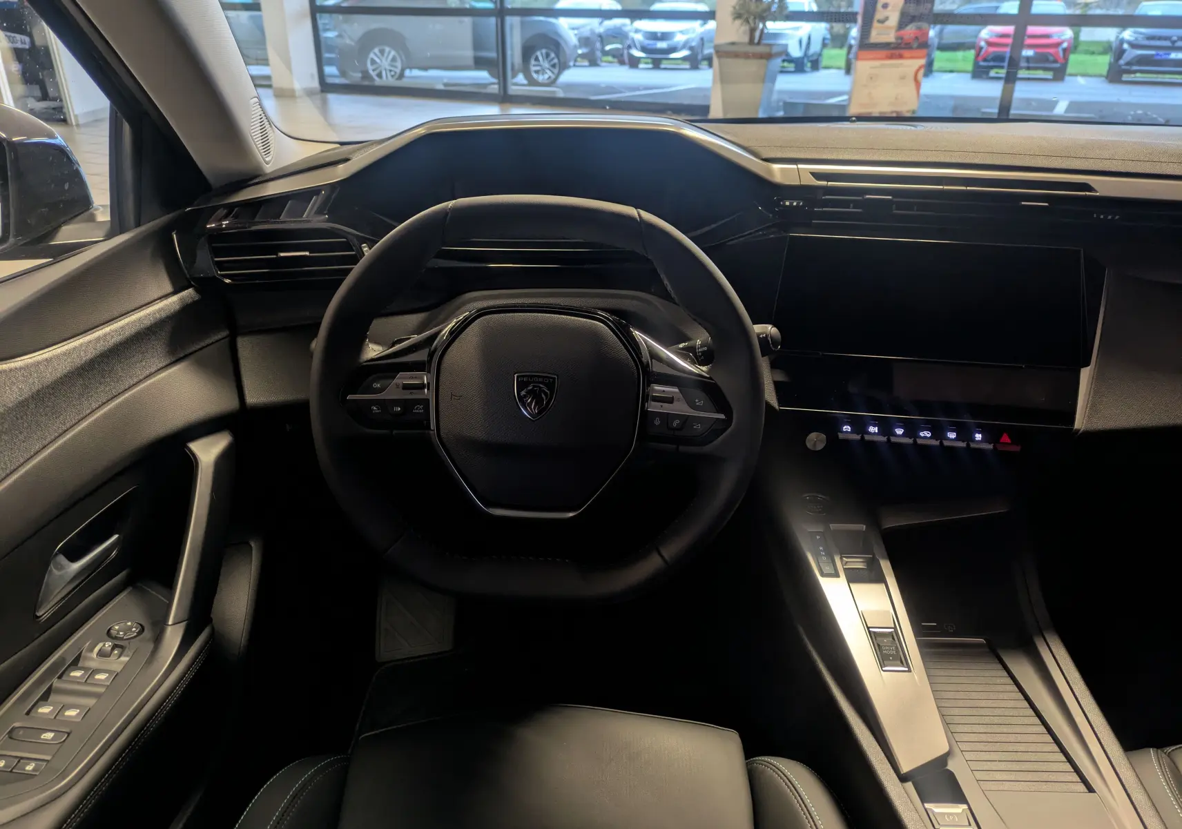 Intérieur de la Peugeot 308 2025 en vue centrée sur le volant, avec tableau de bord moderne et écran tactile noir.
