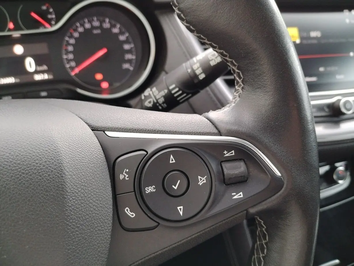 Gros plan sur le volant en cuir noir de l'Opel Grandland X 2019, avec commandes audio et tableau de bord en arrière-plan.