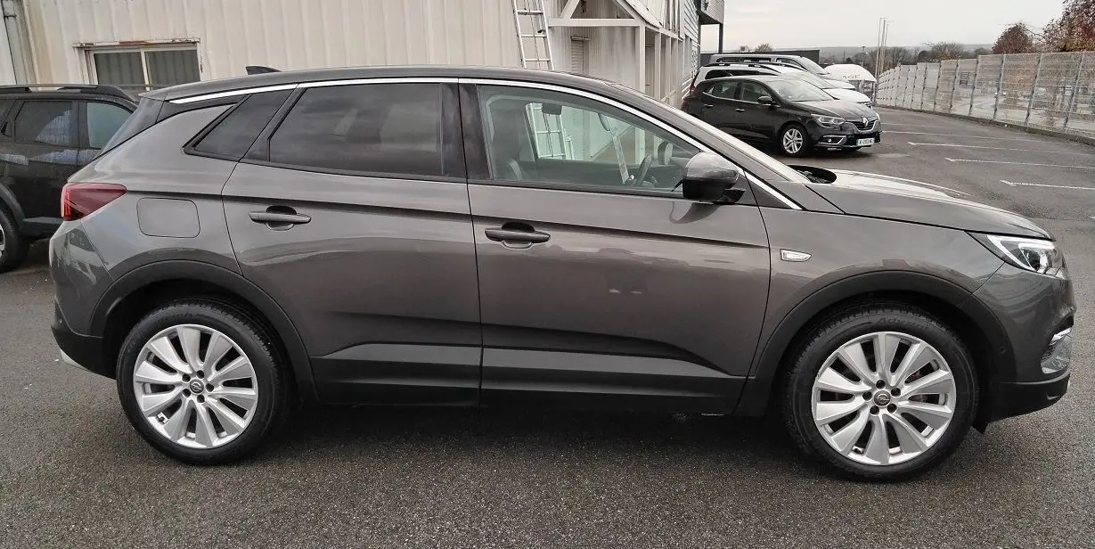 Vue de profil côté gauche d'un Opel Grandland X gris platinium avec jantes alliage et vitres teintées, stationné en extérieur.