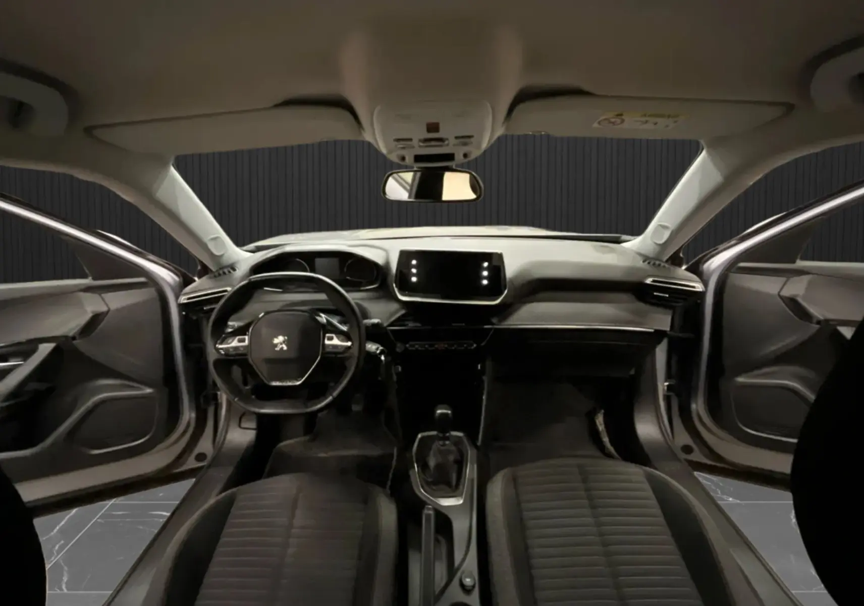 Vue intérieure avant du Peugeot 2008 gris alu 2020, tableau de bord moderne avec écran tactile et portes avant ouvertes.