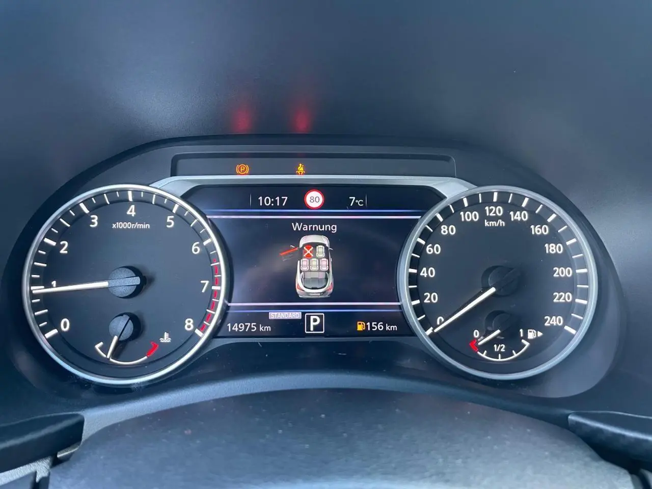 Vue rapprochée du combiné d'instruments digital du Nissan Juke II bleu Magnetic, affichant alertes et compteurs.