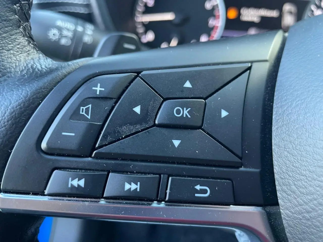 Gros plan sur les commandes au volant noir du Nissan Juke II 2024 en bleu Magnetic, avec boutons multifonctions.