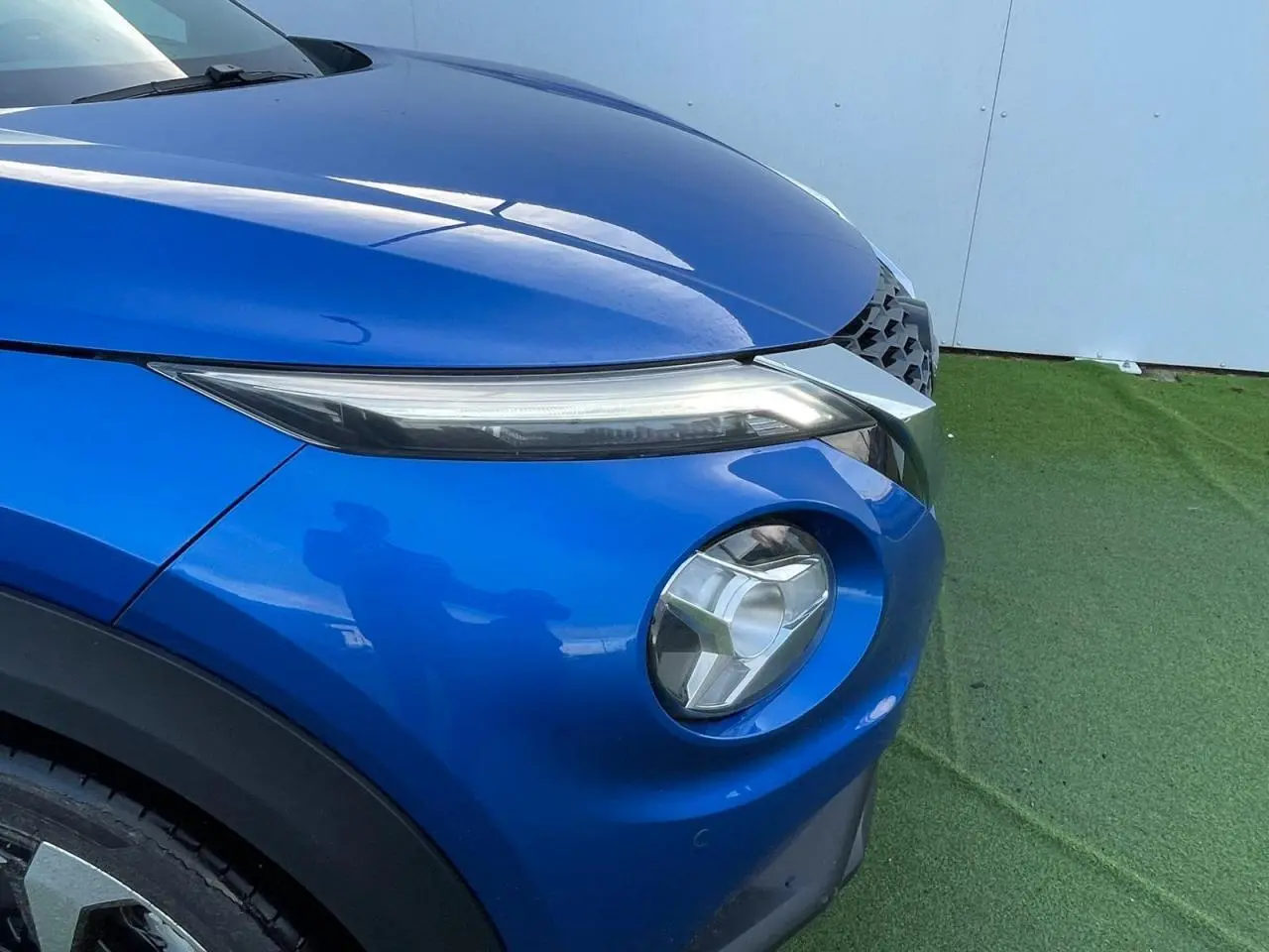 Gros plan sur l'avant droit du Nissan Juke II 2024 en bleu magnetic, mettant en valeur ses phares LED et la calandre noire.