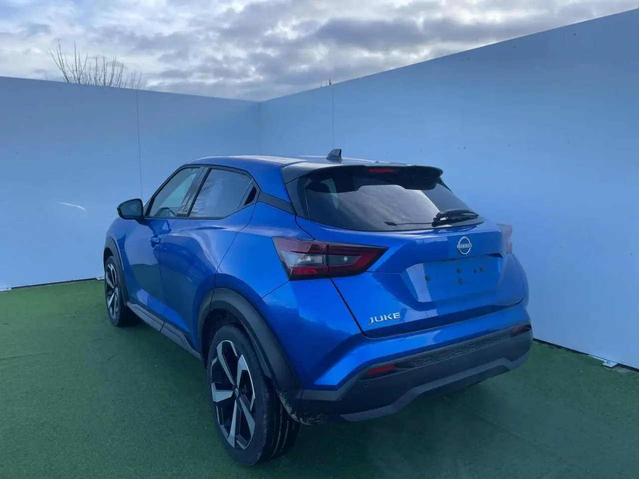 Vue 3/4 arrière gauche du Nissan Juke 2024 bleu magnetic avec toit noir et jantes alliage noires.