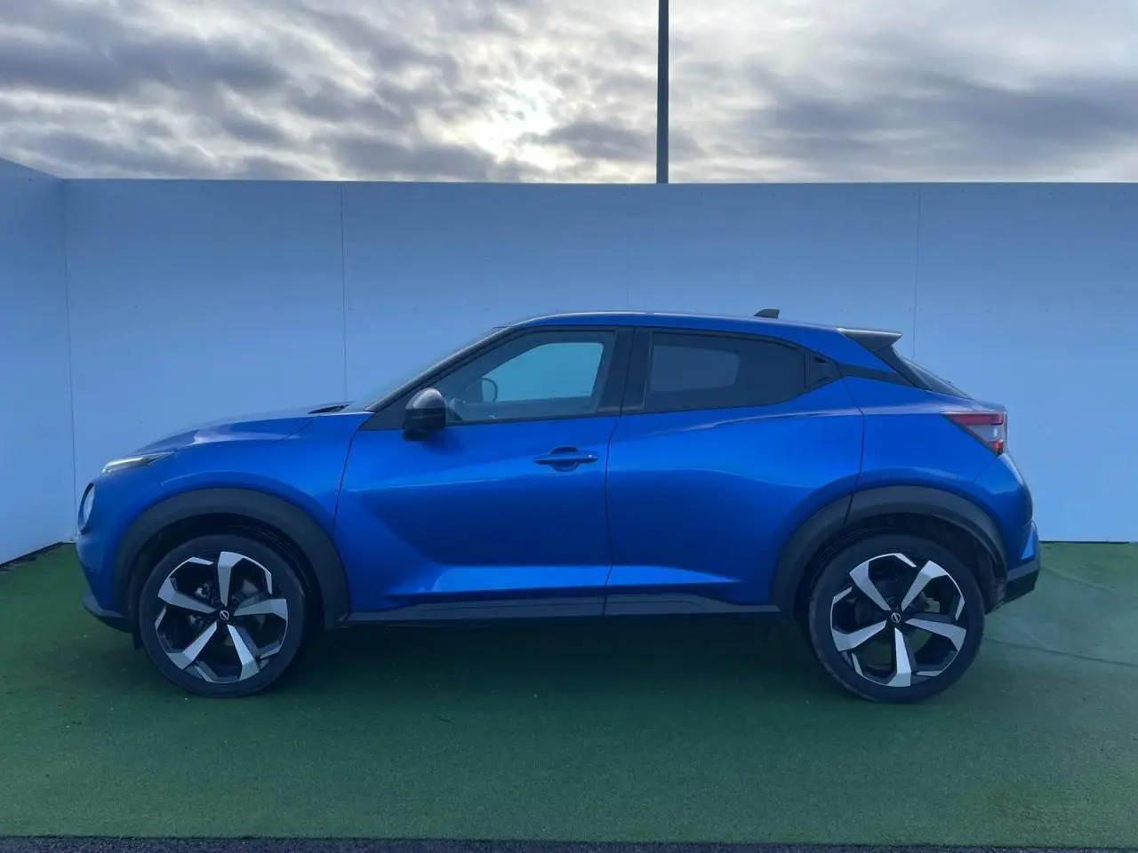 Profil côté gauche du Nissan Juke 2 bleu magnetic 2024 avec jantes alliage noires et vitres teintées.