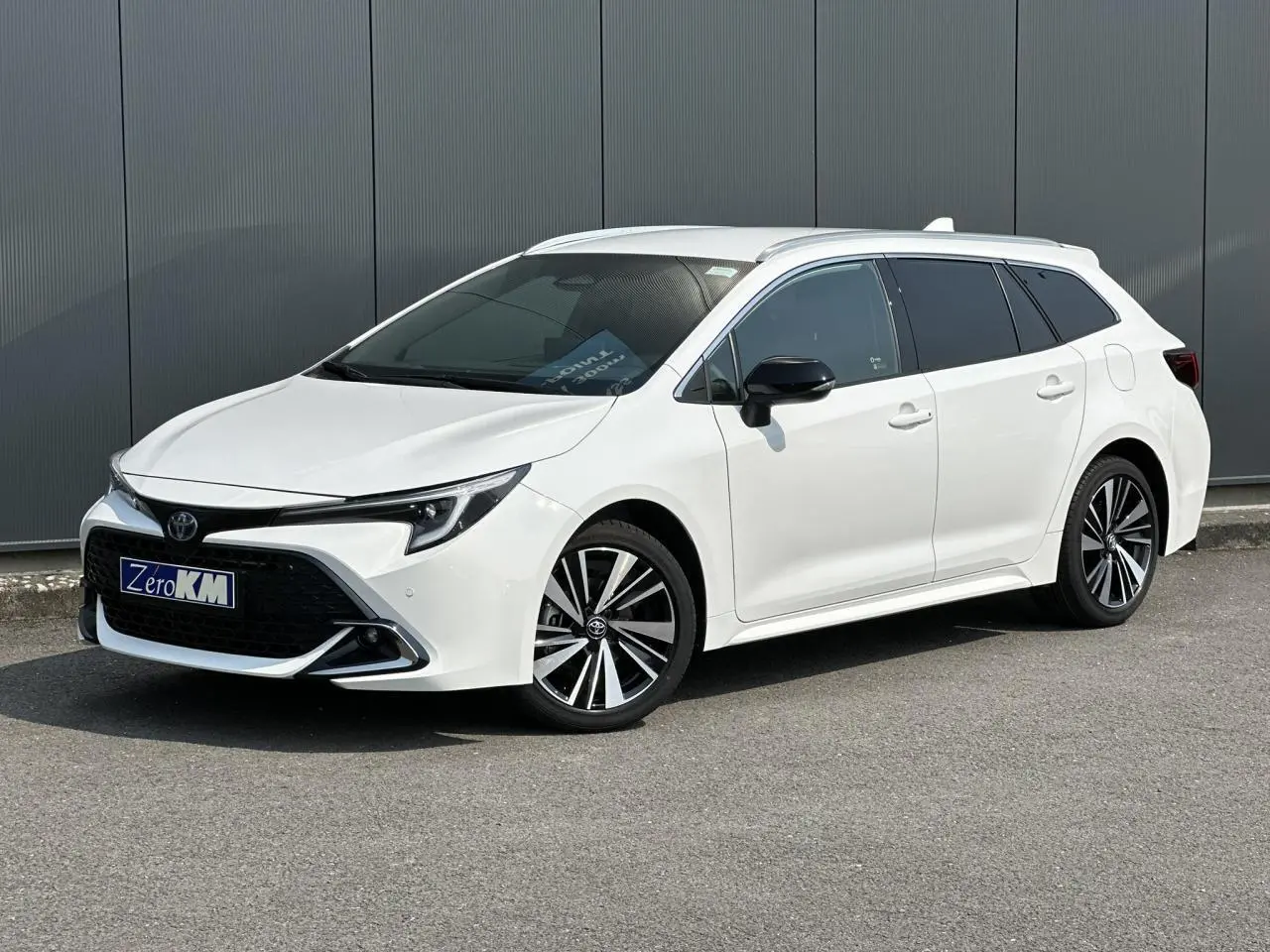 Toyota Corolla Touring Sport blanc neige en vue 3/4 avant droit avec jantes alliage et vitres teintées.