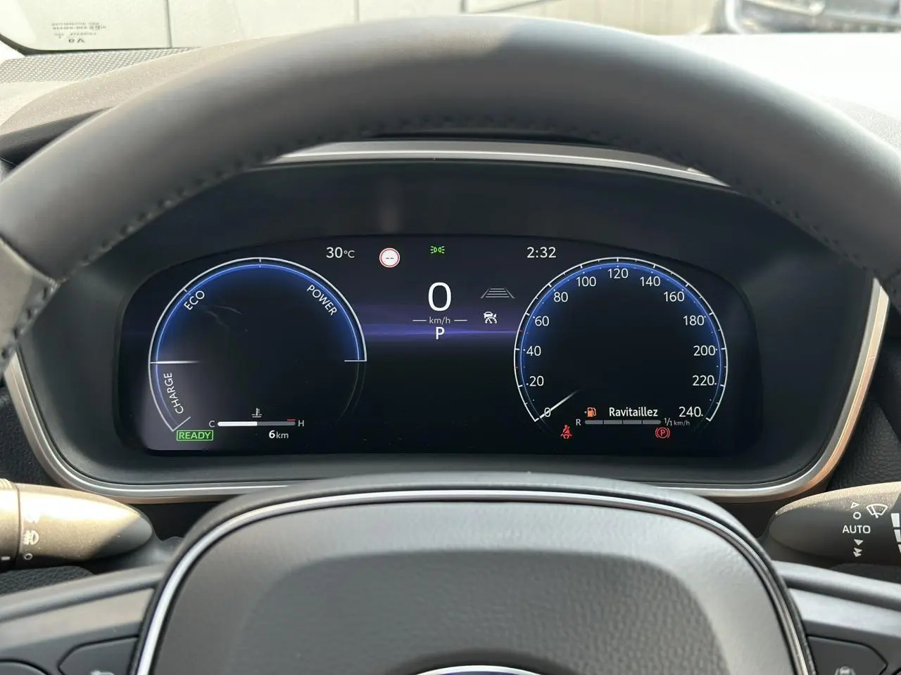 Tableau de bord numérique vu de face dans une Toyota Corolla Touring Sport 1.8 Hybrid 140 Sport blanc, affichage vitesse et énergie hybride.