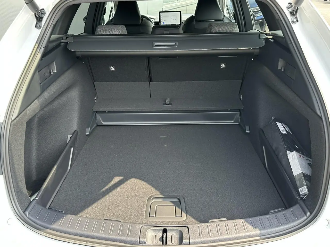 Coffre ouvert vu de l'arrière d'une Toyota Corolla Touring Sport blanc neige, montrant un espace de chargement spacieux et bien fini.