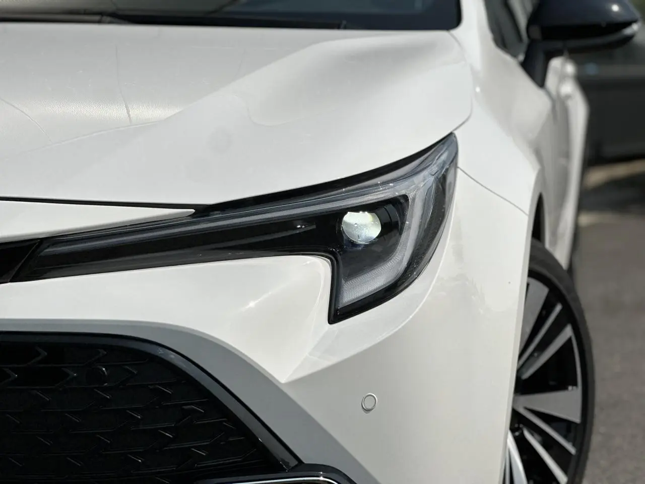 Gros plan sur le phare avant droit d'une Toyota Corolla Touring Sport blanche Neige, avec jante alliage visible.