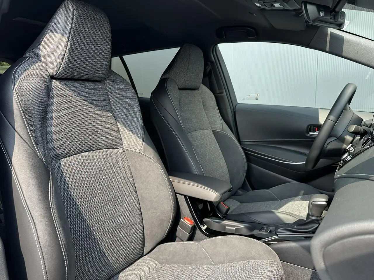 Intérieur de la Toyota Corolla Touring Sport 2025, vue côté droit sur sièges tissu gris et accoudoir central noir.