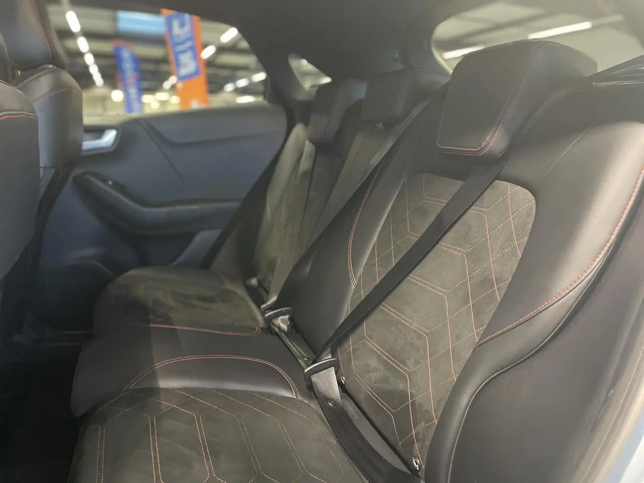 Vue intérieure côté gauche des sièges arrière en suédine et vinyle noir avec surpiqûres rouges du Ford Puma 2024 gris clair.