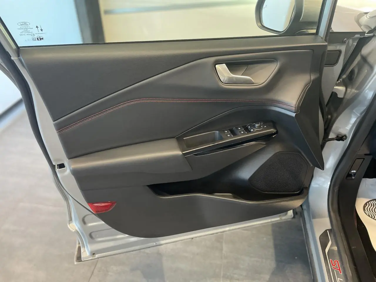 Vue rapprochée de la porte avant gauche du Ford Puma gris clair, avec garniture noire et surpiqûres rouges.