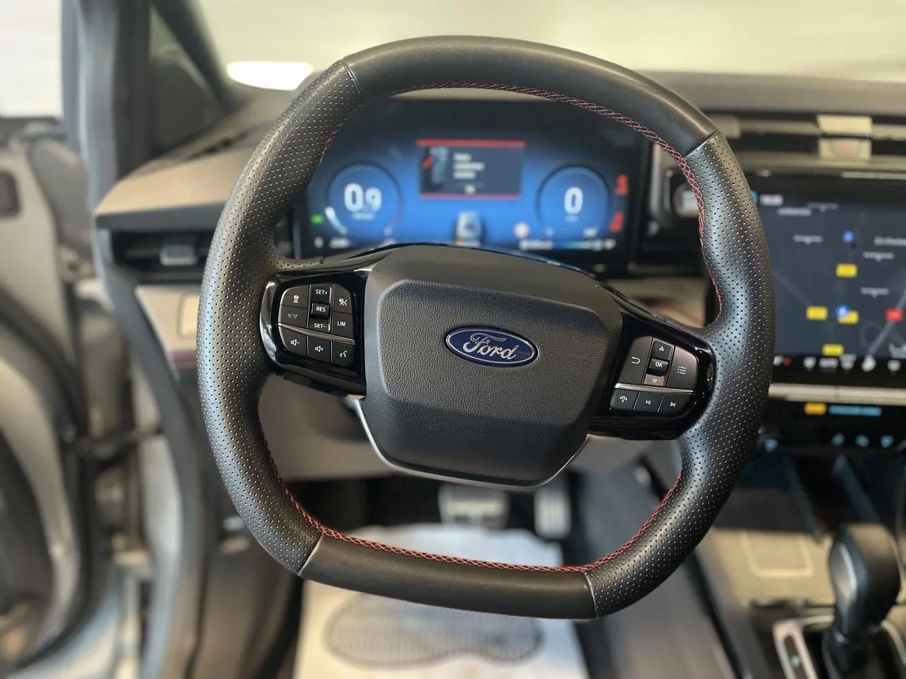 Volant en cuir noir avec surpiqûres rouges du Ford Puma 2024, tableau de bord numérique et écran tactile visibles en arrière-plan.