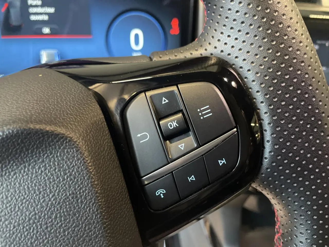 Gros plan sur les commandes multifonctions noires du volant perforé du Ford Puma gris clair 2024.