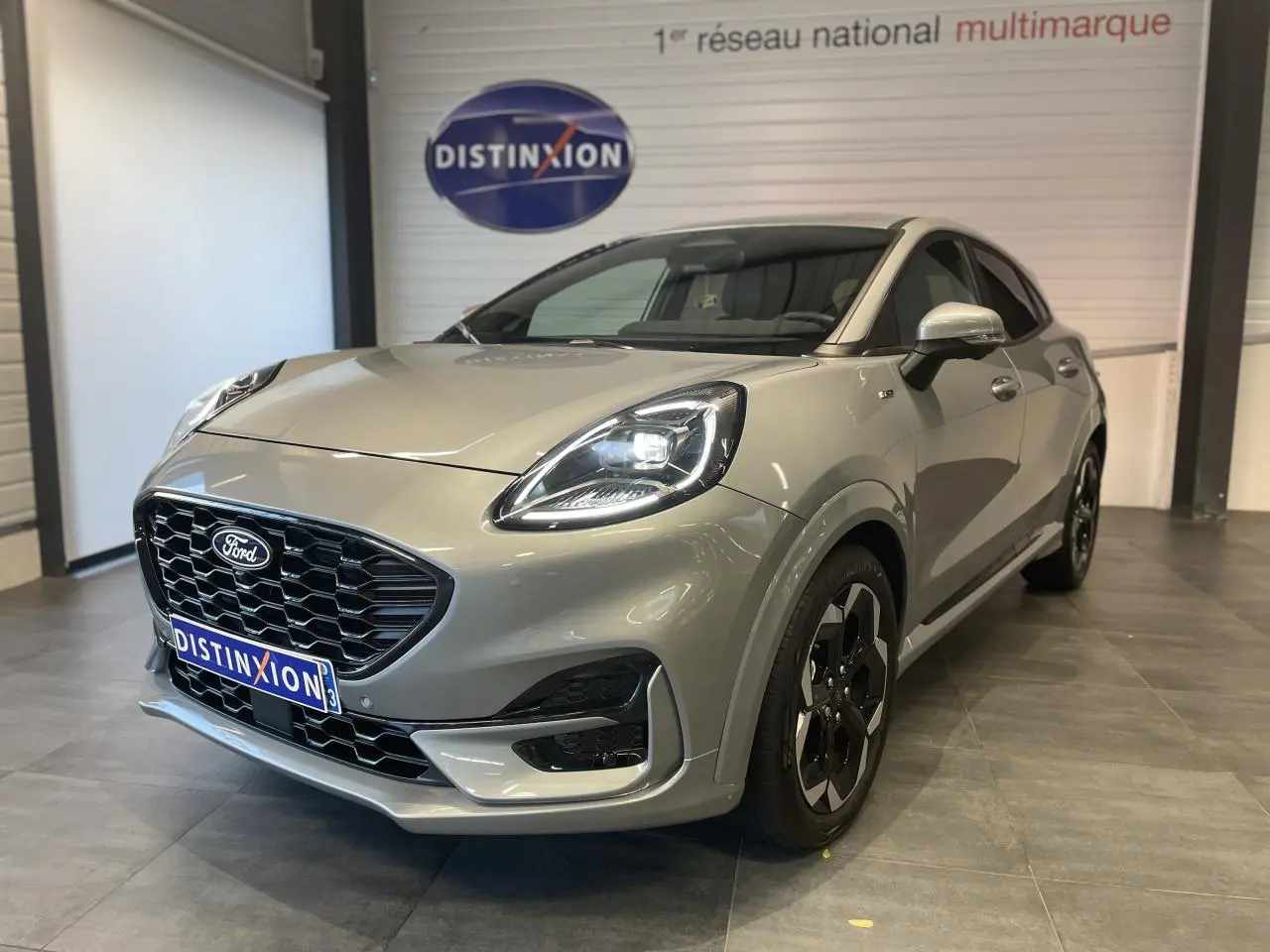 Ford Puma gris clair en 3/4 avant droit, avec calandre noire et jantes alliage noires distinctives.