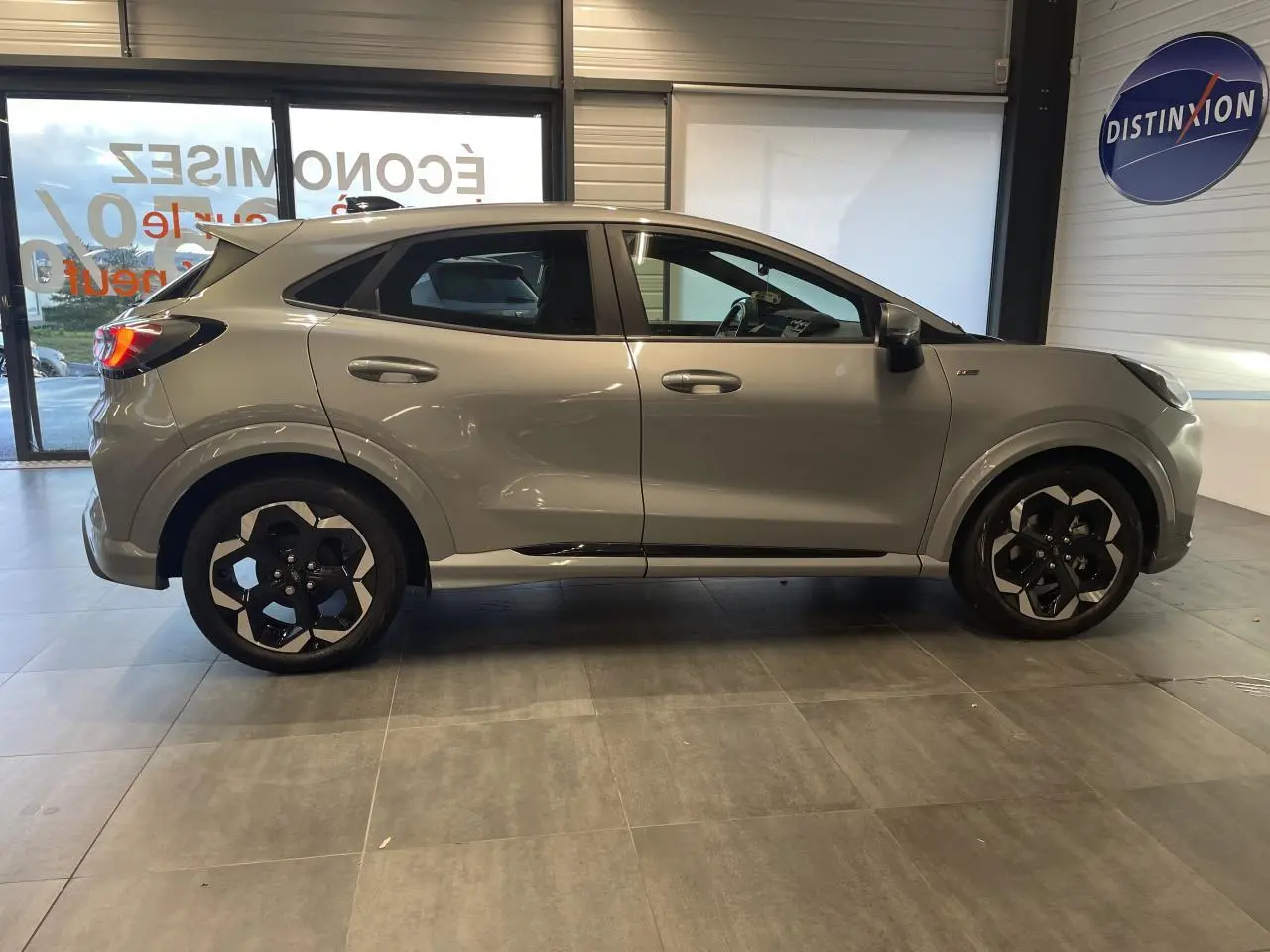 Vue de profil côté gauche d'un Ford Puma gris clair avec jantes alliage noires et détails noirs sur les bas de caisse.