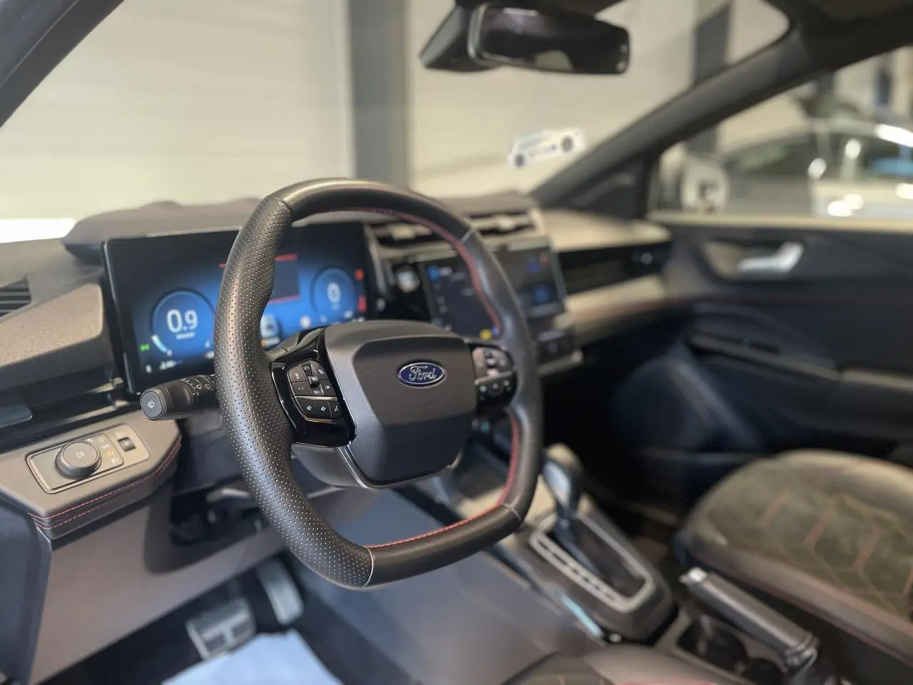 Vue intérieure côté conducteur du Ford Puma 2024, volant cuir noir avec surpiqûres rouges et tableau de bord numérique.