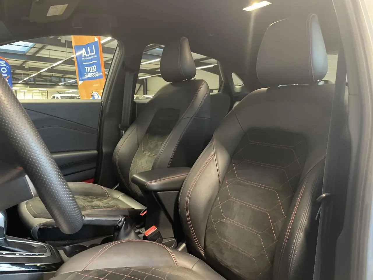 Vue intérieure du côté conducteur du Ford Puma 2024, sièges noirs en suédine et cuir avec surpiqûres rouges visibles.