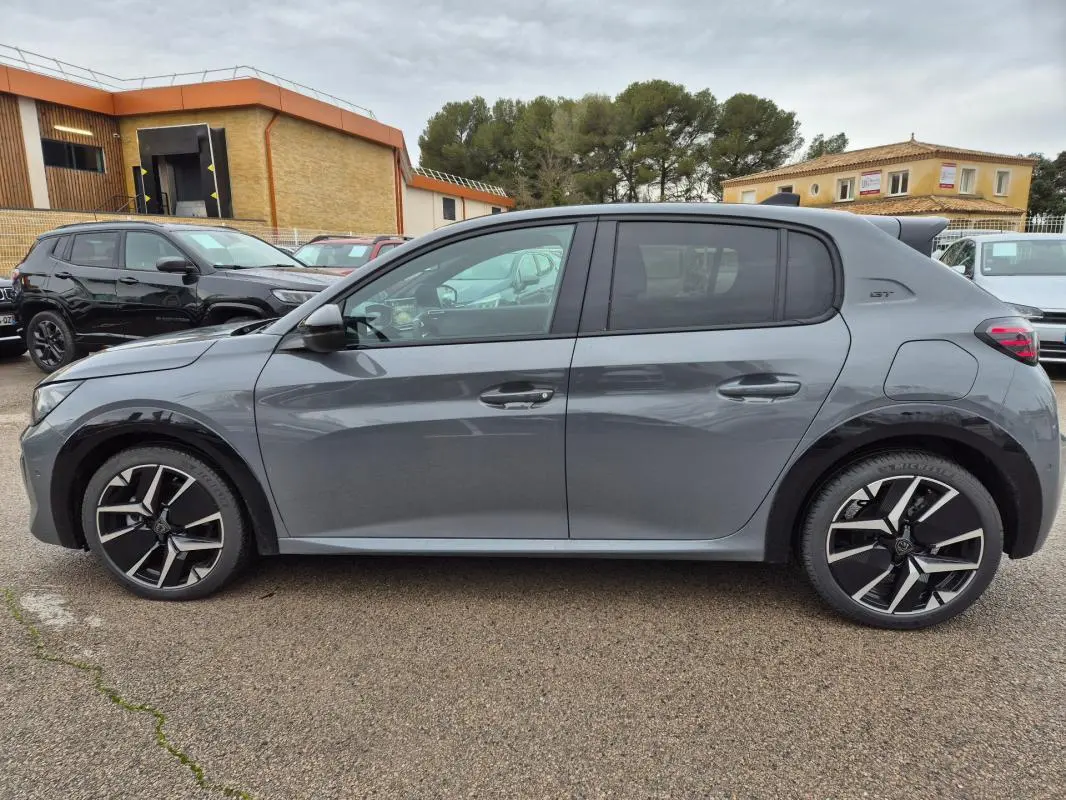 Profil côté gauche d'une Peugeot 208 Hybrid 110 e-DCS6 GT gris avec jantes alliage 17 pouces et antenne requin.